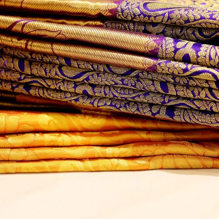 Folded Kanchipuram silk sarees with gold borders, stacked on a shop counter