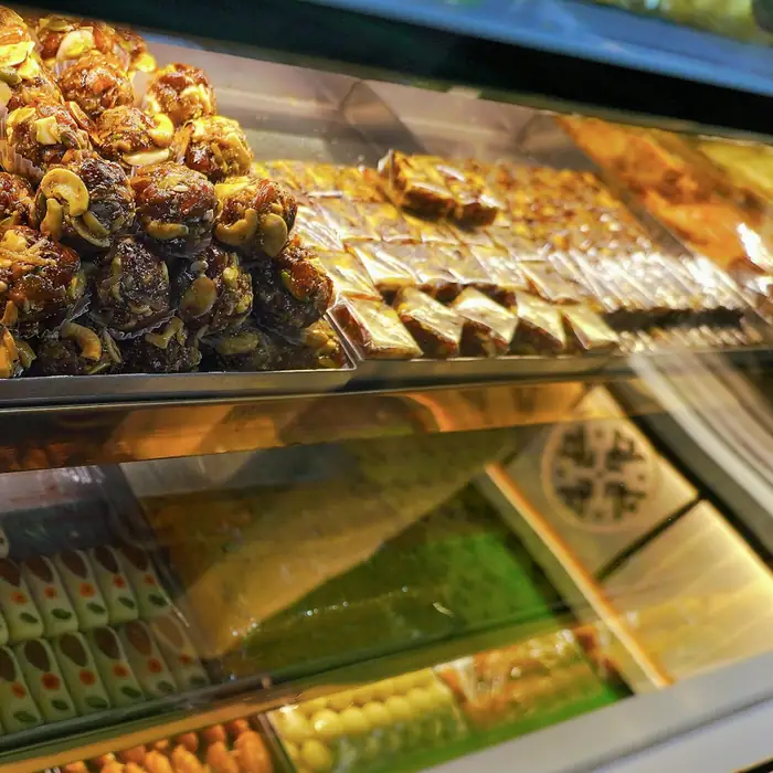 A well-lit sweet shop display: kaju katli with silver leaf, dry-fruit sweets and burfi